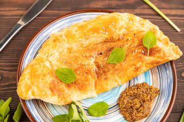 Fried homemade khachapuri cake with cheese and meat, fried in pan on brown wooden. Side view, close up, selective focus