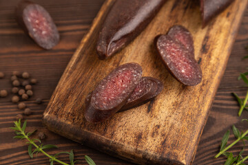 Sujuk sausage on wooden cutting board with pepper and herbs on brown wooden. Side view, selective focus