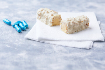 Protein bar in two pieces and amino acids capsules on wooden background. Soft focus. Close up. Copy space