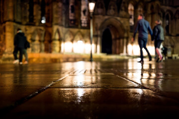 Shallow focus of a wet pavement in the historic city of York, UK. Out of focused people can be seen walking around the famous York Cathedral.