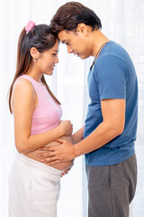 Naklejka premium Asian man touch belly of pregnant woman and stand with attach forehead together express love and care in front of white curtain.