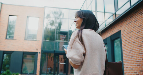 Camera following Caucasian woman with long straight hair. Confidently walking towards building with...