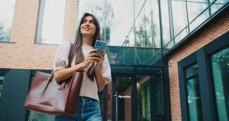 Beautiful Caucasian woman walking in city. Going somewhere for evening. Using her smartphone....