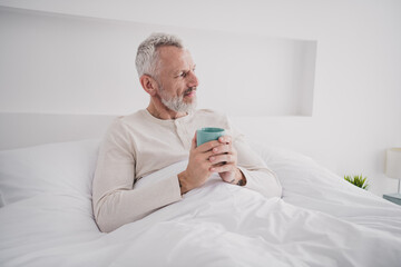 Elderly man enjoying a peaceful morning in bed with a warm beverage