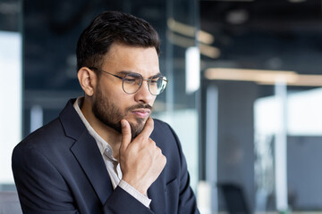 A thoughtful businessman in a suit, deep in contemplation, reflects serious decision-making in a modern office setting. This image captures professional focus and critical thinking.