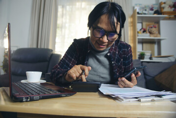 Season to pay Tax and Budget planning concept. Business woman calculating annual tax and using mobile phone, calculator, personal income tax form, cup of coffee, and laptop placed on home office desk.