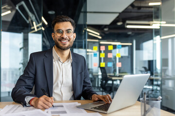 Young professional in a suit enthusiastically working on his laptop at an office desk. Bright...