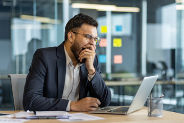 A professional man yawning as he works on his laptop, showcasing fatigue in a contemporary office...