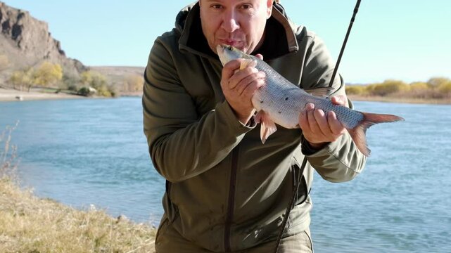 A fisherman holds a fish in his hands and rejoices at his catch. An adult fisherman stands with an asp and shows it to the camera, the fish moves in the frame, the man kisses the fish.
