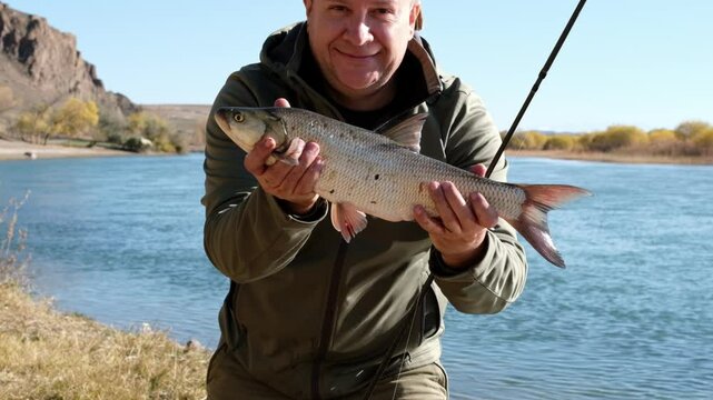 A fisherman holds a fish in his hands and rejoices at his catch. An adult fisherman stands with an asp and shows it to the camera, the fish moves in the frame, the man kisses the fish.