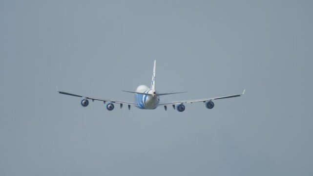Footage rear view of heavy four-engine cargo aircraft gaining altitude after takeoff. Airliner in the sky. Airplane flying away