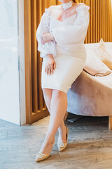 A woman elegantly dressed in a stunning white dress is comfortably sitting on a plush couch,...