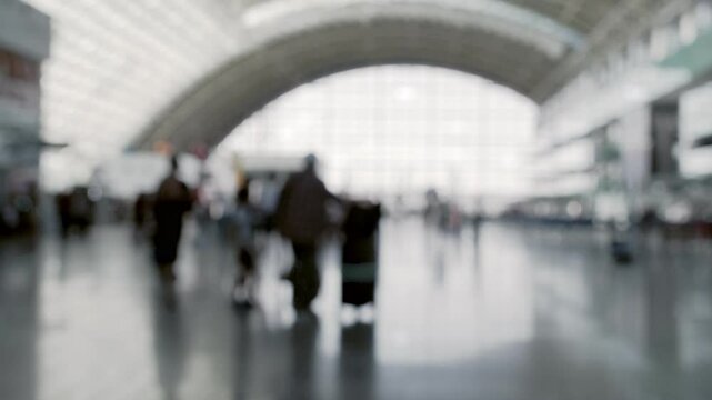 A blurred image capturing passengers with suitcases walking through a modern airport terminal. The silhouettes and soft focus evoke a sense of movement and travel