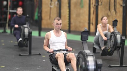 Concentrated young adult man doing high intensity full body workout in gym, exercising on rowing machine . High quality 4k footage