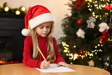 Little girl writing letter to Santa Claus at table indoors. Christmas celebration