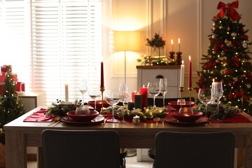 Christmas table setting with stylish dishware, glasses and burning candles in festive decorated room