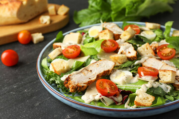Tasty Caesar salad with chicken and tomatoes on dark gray textured table, closeup
