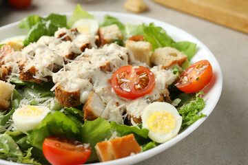Tasty Caesar salad with chicken and tomatoes in bowl on gray textured table, closeup