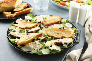 Delicious Caesar salad with chicken on grey textured table, closeup