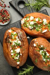 Tasty cooked sweet potatoes with feta cheese, green onion, parsley and spices on gray textured table, flat lay