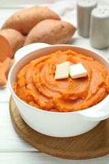 Tasty mashed sweet potato with butter in bowl on white wooden table, closeup