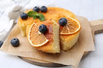 Pieces of delicious semolina cake with blueberries and orange slices on white tiled table, closeup