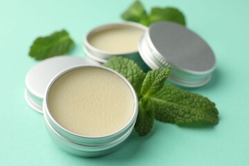 Natural lip balms and mint leaves on turquoise background, closeup