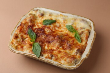 Delicious cooked lasagna in baking dish and basil on pale brown background, closeup