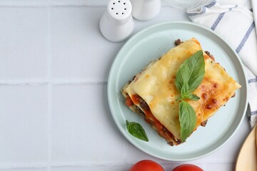 Delicious cooked lasagna with basil served on white tiled table, flat lay. Space for text