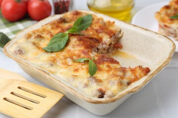 Delicious cooked lasagna with basil in baking dish on white table, closeup