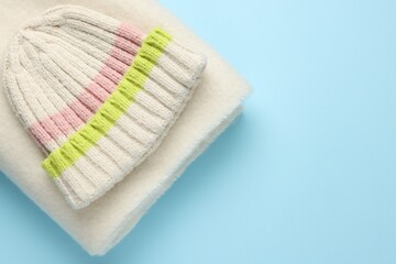 Warm woolen hat and scarf on light blue background, top view. Space for text