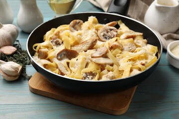 Tasty Alfredo pasta with chicken and mushrooms in frying pan on light blue wooden table, closeup