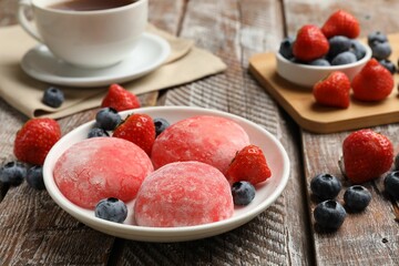 Delicious mochi, strawberries, blueberries and tea on wooden table, closeup