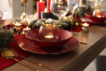 Christmas place setting with festive decor on wooden table in room, closeup