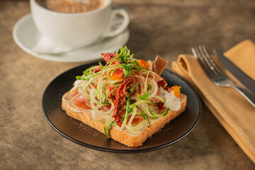 A close-up of a gourmet toast topped with fresh vegetables, prosciutto, cream