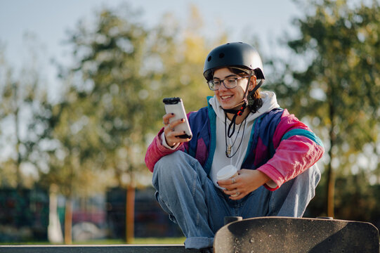 Smiling skater using smartphone and holding coffee in skate park
