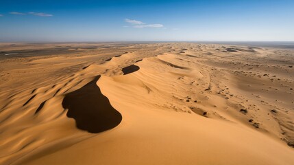 Expansive desert landscape with rolling sand dunes under a clear blue sky.