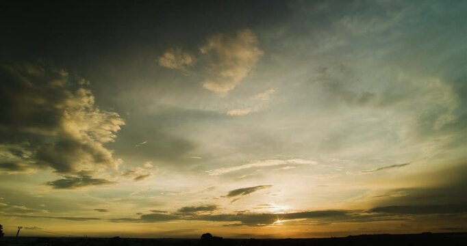 Timelapse of wide angle view of beautiful sunset sky with different layers of clouds moving in opposite directions and showing off interesting slowly changing shapes and magical warm colors