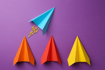 Light blue paper plane bursting forward among others on purple background