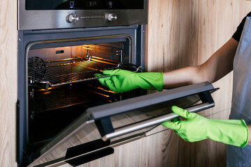 Woman cleaning modern oven in a bright kitchen at home