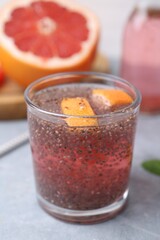 Glass of drink with chia seeds and grapefruit on grey table, closeup