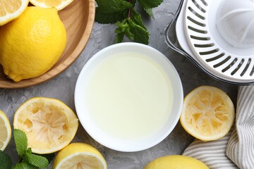 Fresh lemon juice in bowl, fruits, mint and juicer on grey table, top view