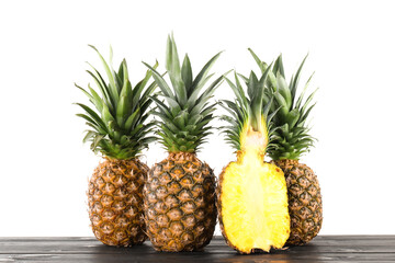 Whole and cut ripe pineapples on wooden table against white background