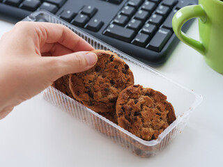 A businesswoman taking a chocolate chip cookie from a box of other ones and getting ready to eat it during a break at work. Close up.