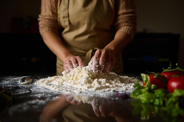 Person preparing dough with fresh vegetables on a kitchen counter