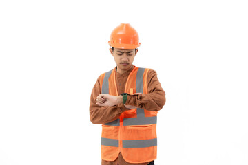 Young Indonesian male construction worker in full safety gear looking tired looking at time on his watch, industrial and construction concept, isolated on white background.