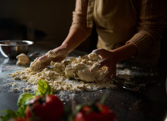 Person kneading dough on a kitchen surface with fresh tomatoes