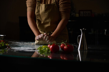 Person kneading dough on a kitchen counter surrounded by fresh vegetables