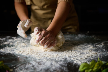 Close-up of hands kneading dough on floured kitchen counter