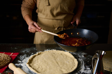 Woman preparing homemade pizza with sauce in a cozy kitchen setting